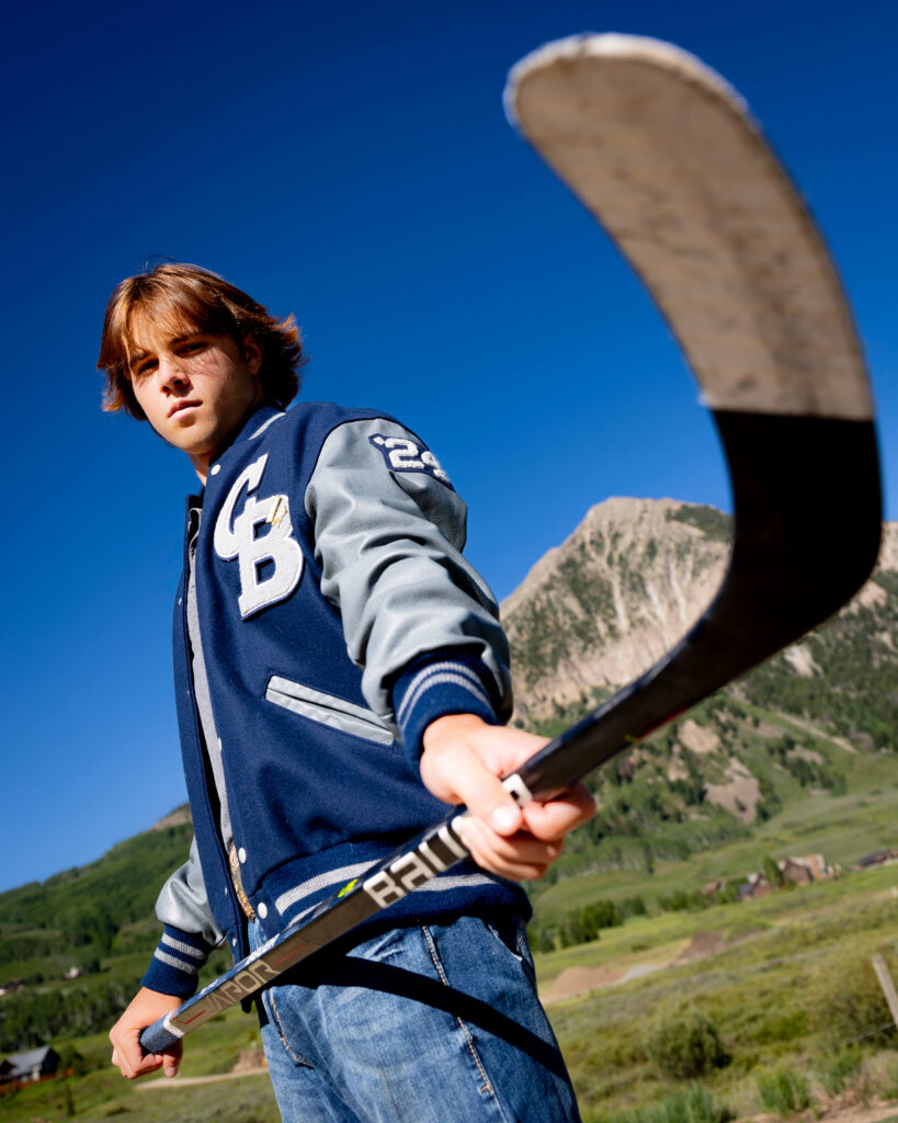 Young man with a hockey stick and Mt. Crested Butte in the background for his senior pictures.
