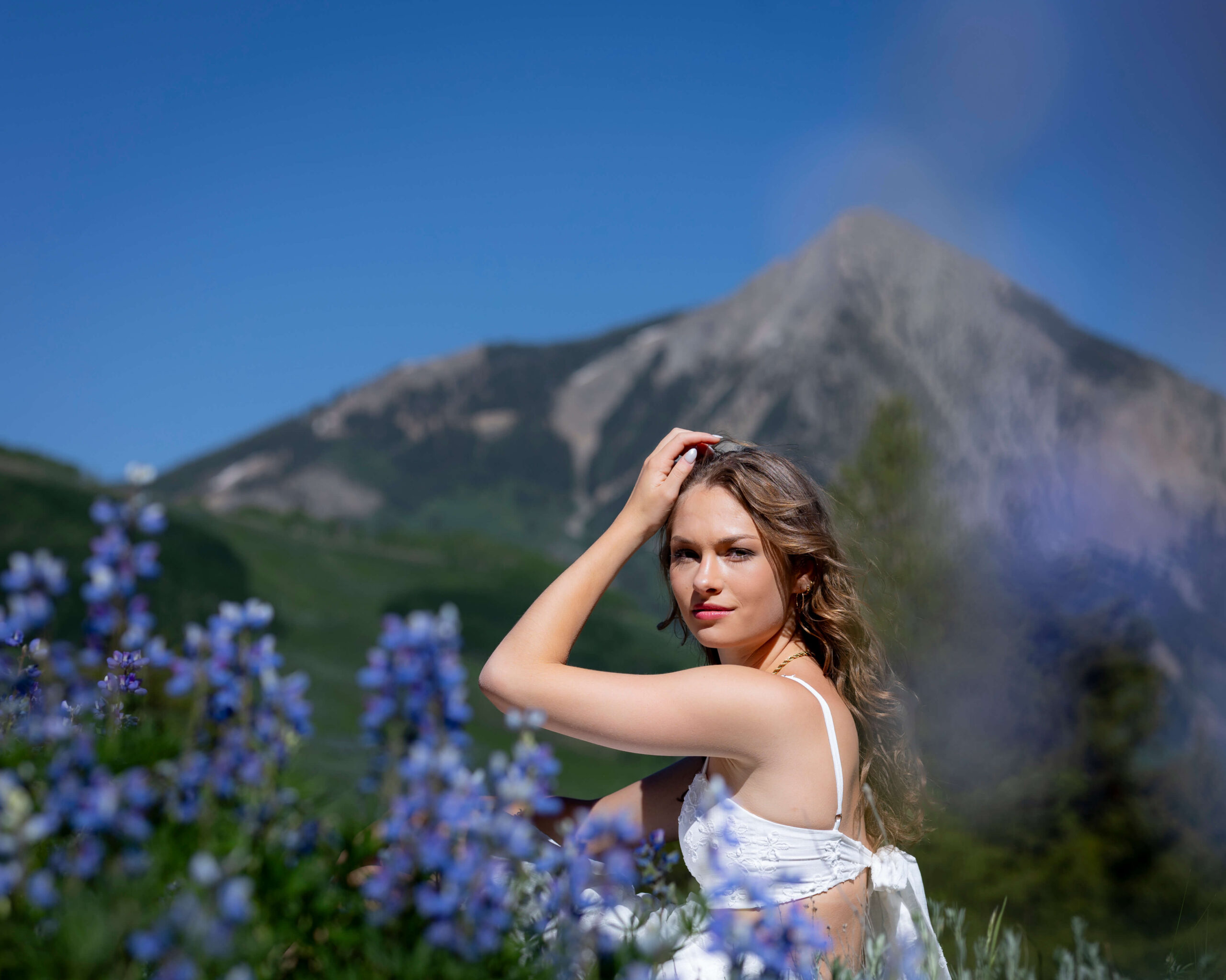 Woman in a white dress posing in a field of blue flowers with a mountain in the background